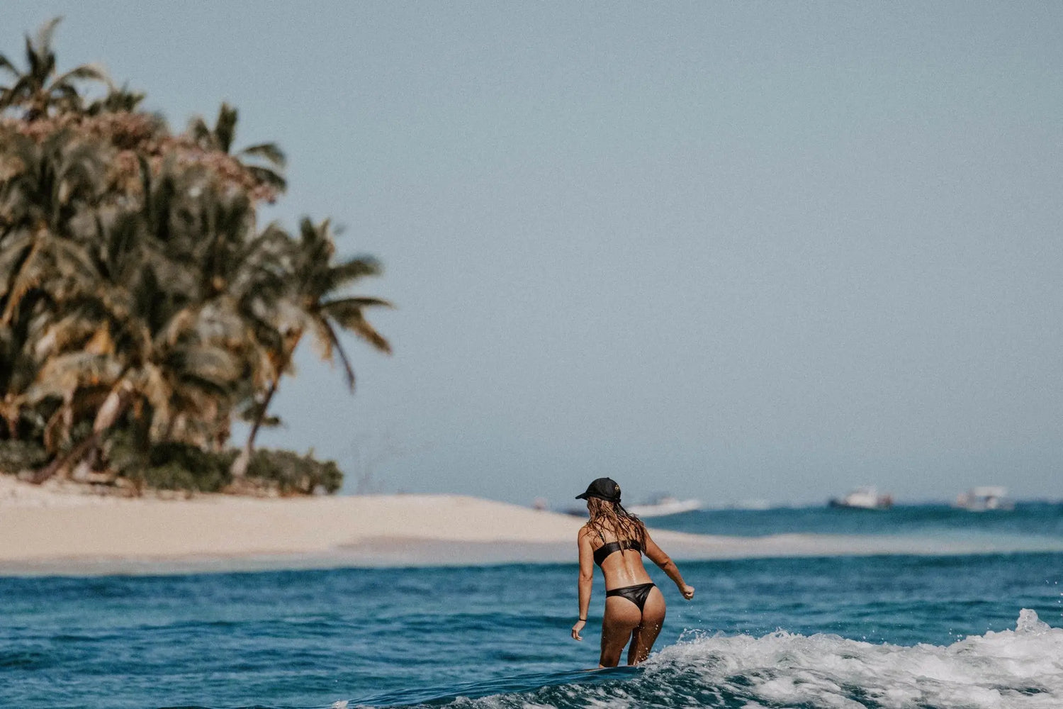 Woman surfing wearing our Iluka Swim Top and Tau Swim Bottom in Black