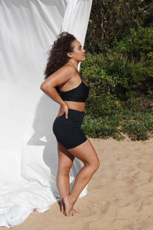 Model at the beach facing the side wearing our Inala Crop and Allawah Short in Black